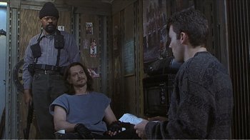 Movie still from “Reindeer Games” (2000), directed by John Frankenheimer – A man sitting in front of another man in front of a television; Medium shot, Over the shoulder angle