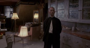 Movie still from “Remo Williams: The Adventure Begins” (1985), directed by Guy Hamilton – A man standing in a living room with a lamp; Medium shot, Low angle