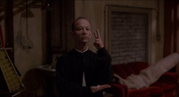 Movie still from “Remo Williams: The Adventure Begins” (1985), directed by Guy Hamilton – A man in a black shirt is making a peace sign with his hand; Medium shot, Low angle