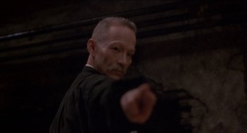 Movie still from “Remo Williams: The Adventure Begins” (1985), directed by Guy Hamilton – A man with a shaved head is pointing at the camera; Close Up shot, Low angle