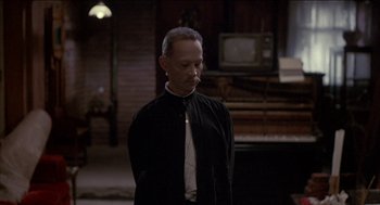 Movie still from “Remo Williams: The Adventure Begins” (1985), directed by Guy Hamilton – A man wearing a black robe standing next to a piano; Medium shot, Over the shoulder angle