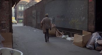Movie still from “Remo Williams: The Adventure Begins” (1985), directed by Guy Hamilton – A man walking down a street with a bag of trash; Wide shot, High angle