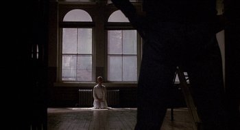 Movie still from “Remo Williams: The Adventure Begins” (1985), directed by Guy Hamilton – A man is standing in front of two large windows in a room; Wide shot, Over the shoulder angle