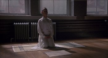 Movie still from “Remo Williams: The Adventure Begins” (1985), directed by Guy Hamilton – A man sitting on the ground in a room; Wide shot, High angle