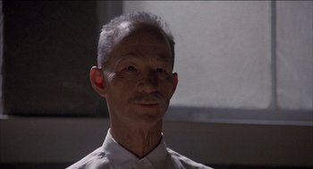 Movie still from “Remo Williams: The Adventure Begins” (1985), directed by Guy Hamilton – An old man with a shaved head and a white shirt; Close Up shot, Low angle