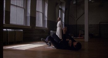 Movie still from “Remo Williams: The Adventure Begins” (1985), directed by Guy Hamilton – A man and a woman are in a room with windows; Wide shot, Low angle