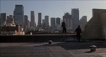 Movie still from “Remo Williams: The Adventure Begins” (1985), directed by Guy Hamilton – Two people standing on the edge of a building; Extreme Wide shot, Low angle