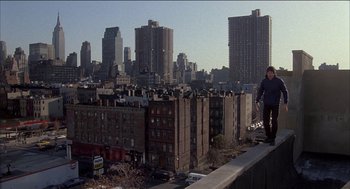 Movie still from “Remo Williams: The Adventure Begins” (1985), directed by Guy Hamilton – A man standing on the edge of a building on a ledge; Extreme Wide shot, High angle