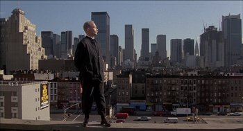 Movie still from “Remo Williams: The Adventure Begins” (1985), directed by Guy Hamilton – A man standing on the roof of a building looking out at a city; Wide shot, Low angle