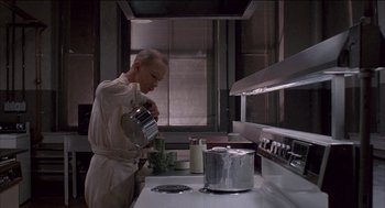 Movie still from “Remo Williams: The Adventure Begins” (1985), directed by Guy Hamilton – A man in a kitchen preparing food in a pot; Medium shot, Low angle