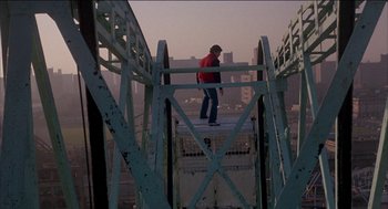 Movie still from “Remo Williams: The Adventure Begins” (1985), directed by Guy Hamilton – A man standing on top of a metal structure; Wide shot, High angle