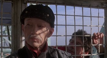 Movie still from “Remo Williams: The Adventure Begins” (1985), directed by Guy Hamilton – An old man wearing a black hat and a black jacket; Close Up shot, Low angle