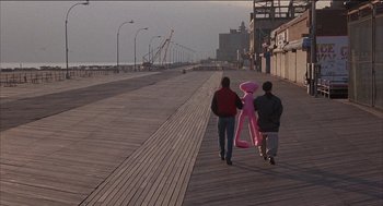 Movie still from “Remo Williams: The Adventure Begins” (1985), directed by Guy Hamilton – Two people walking down a boardwalk with a large pink balloon; Wide shot, High angle