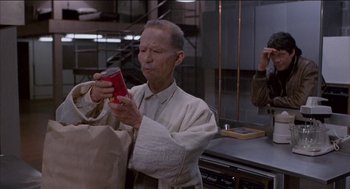 Movie still from “Remo Williams: The Adventure Begins” (1985), directed by Guy Hamilton – An older man holding a red bag and looking at his cell phone; Medium shot, High angle
