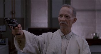 Movie still from “Remo Williams: The Adventure Begins” (1985), directed by Guy Hamilton – An older man is holding his arm up; Close Up shot, Low angle