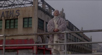 Movie still from “Remo Williams: The Adventure Begins” (1985), directed by Guy Hamilton – An old man standing in front of an abandoned building; Wide shot, Low angle