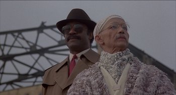 Movie still from “Remo Williams: The Adventure Begins” (1985), directed by Guy Hamilton – A man and a woman standing next to each other; Close Up shot, Low angle
