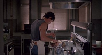 Movie still from “Remo Williams: The Adventure Begins” (1985), directed by Guy Hamilton – A man in an apron is cooking in a kitchen; Medium shot, Low angle