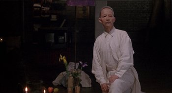 Movie still from “Remo Williams: The Adventure Begins” (1985), directed by Guy Hamilton – An older man sitting in front of a vase of flowers; Medium shot, Low angle