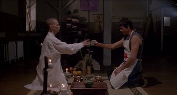 Movie still from “Remo Williams: The Adventure Begins” (1985), directed by Guy Hamilton – Two men in aprons are holding hands over a table; Medium shot, Low angle