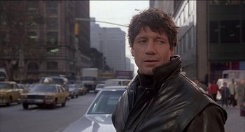 Movie still from “Remo Williams: The Adventure Begins” (1985), directed by Guy Hamilton – A man standing in the middle of a street; Close Up shot, Low angle