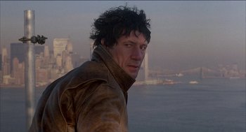 Movie still from “Remo Williams: The Adventure Begins” (1985), directed by Guy Hamilton – A man in a brown jacket is looking at the camera; Close Up shot, Low angle