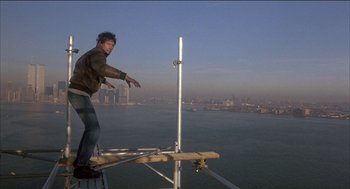 Movie still from “Remo Williams: The Adventure Begins” (1985), directed by Guy Hamilton – A man standing on top of a metal structure; Wide shot, Low angle