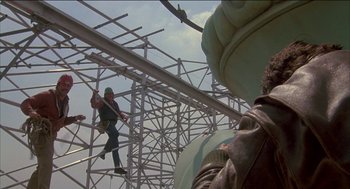 Movie still from “Remo Williams: The Adventure Begins” (1985), directed by Guy Hamilton – A man on a metal structure climbing up a metal structure; Wide shot, Low angle