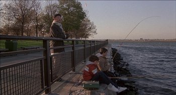 Movie still from “Remo Williams: The Adventure Begins” (1985), directed by Guy Hamilton – Two people fishing on a pier next to a body of water; Wide shot, Over the shoulder angle