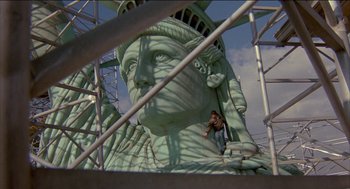 Movie still from “Remo Williams: The Adventure Begins” (1985), directed by Guy Hamilton – A man riding a skate board on top of a statue of liberty; Extreme Wide shot, Low angle