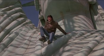 Movie still from “Remo Williams: The Adventure Begins” (1985), directed by Guy Hamilton – A man sitting on top of a statue of liberty; Wide shot, Low angle
