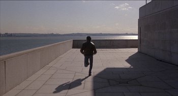 Movie still from “Remo Williams: The Adventure Begins” (1985), directed by Guy Hamilton – A man is running on a walkway near the water; Wide shot, High angle