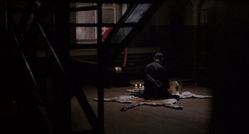 Movie still from “Remo Williams: The Adventure Begins” (1985), directed by Guy Hamilton – A man sitting on the floor in front of candles; Wide shot, High angle