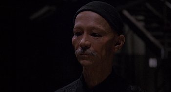 Movie still from “Remo Williams: The Adventure Begins” (1985), directed by Guy Hamilton – An older man with a mustache and a black hat; Close Up shot, Low angle