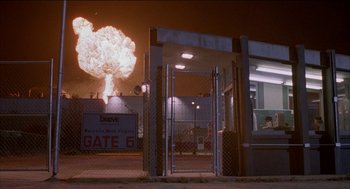 Movie still from “Remo Williams: The Adventure Begins” (1985), directed by Guy Hamilton – An entrance to a gate 6 with an explosion in the background; Extreme Wide shot, Low angle