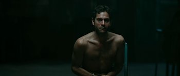 Movie still from “Rendition” (2007), directed by Gavin Hood – A shirtless man sitting in a chair in a dark room; Medium shot, Low angle
