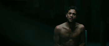 Movie still from “Rendition” (2007), directed by Gavin Hood – A man with no shirt is sitting in a dark room; Medium shot, Low angle