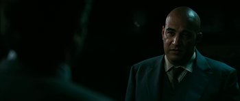 Movie still from “Rendition” (2007), directed by Gavin Hood – A man wearing a suit and tie standing in front of a dark background; Close Up shot, Over the shoulder angle