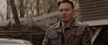 Movie still from “Rhymes for Young Ghouls” (2013), directed by Jeff Barnaby – A man in a brown jacket standing in front of a fence; Close Up shot, Over the shoulder angle