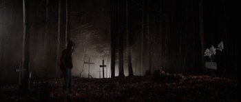 Movie still from “Rhymes for Young Ghouls” (2013), directed by Jeff Barnaby – A person standing in front of a cross in the woods; Wide shot, Over the shoulder angle