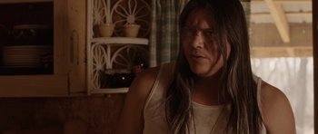 Movie still from “Rhymes for Young Ghouls” (2013), directed by Jeff Barnaby – A man with long black hair is looking at the camera; Close Up shot, Over the shoulder angle