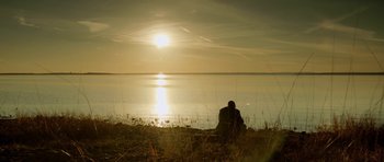 Movie still from “Rhymes for Young Ghouls” (2013), directed by Jeff Barnaby – A man sitting on the beach looking out at the water; Extreme Wide shot, Low angle