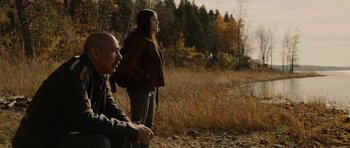 Movie still from “Rhymes for Young Ghouls” (2013), directed by Jeff Barnaby – A man and a woman standing on a dirt field; Medium shot, Low angle