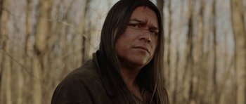 A man with long black hair is looking into the distance