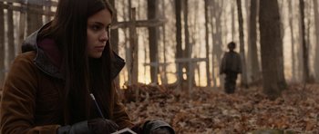 Movie still from “Rhymes for Young Ghouls” (2013), directed by Jeff Barnaby – A woman sitting on the ground in the woods; Medium shot, Over the shoulder angle