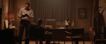 Movie still from “Rhymes for Young Ghouls” (2013), directed by Jeff Barnaby – A man sitting in front of a computer in a darkened room; Wide shot, Over the shoulder angle
