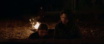 Movie still from “Rhymes for Young Ghouls” (2013), directed by Jeff Barnaby – A woman and a girl sitting next to a fire; Medium shot, Over the shoulder angle