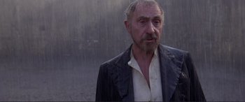 Movie still from “Richard III” (1995), directed by Richard Loncraine – An older man in a black jacket standing in the rain; Medium shot, Over the shoulder angle
