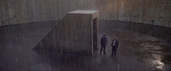 Movie still from “Richard III” (1995), directed by Richard Loncraine – Two men standing in the rain in front of a building; Extreme Wide shot, Overhead angle