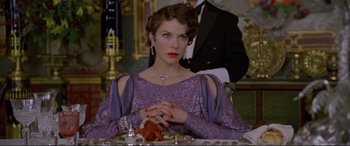 Movie still from “Richard III” (1995), directed by Richard Loncraine – A woman sitting at a table with a man standing in the background; Medium shot, Over the shoulder angle
